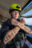 Crewmitglied mit gelben Helm auf dem Kopf, dem Schriftzug "Saving Lives is Not a Crime" auf den Armen, die vor der Brus gekreuzt sind an Bord der Humanity 1.