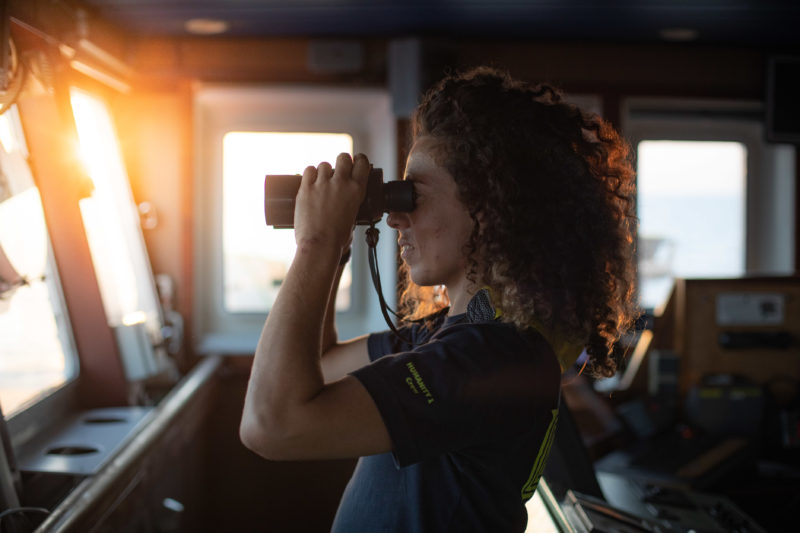 Matrosin Eva auf der Brücke des Rettungsschiffes der Humanity 1 beim Ausschauhalten mit Fernglas