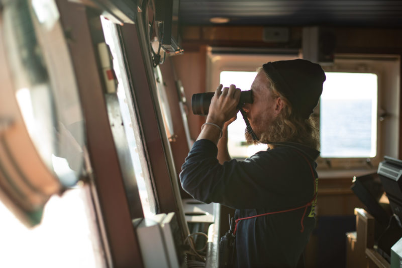 Care Koordinator David mit Fernglas auf der Brücke der Humanity 1