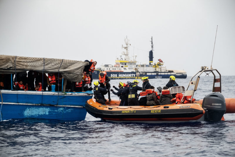 Geflüchtete Personen bei der Rettung von einem blauen Holzboot auf das RHIB der Humanity 1, das Rettungsboot von SOS Humanity.