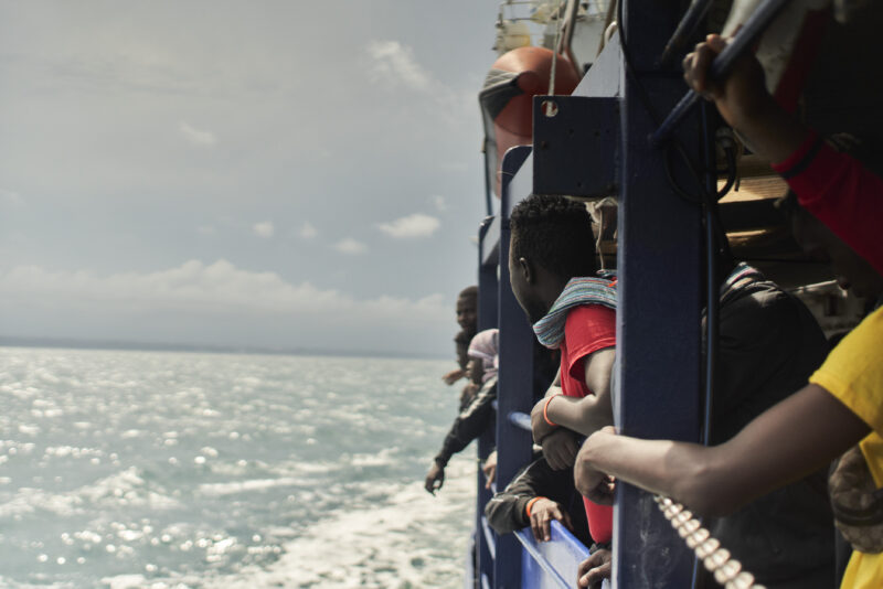 Gerettete und Crew-Mitlgieder blicken aus den Fenstern der Humanity 1 auf das Meer Richtung Italien.