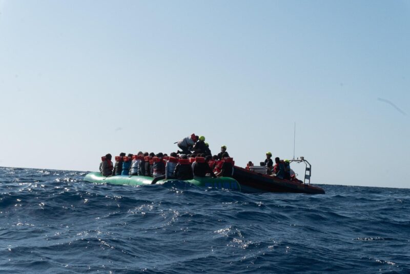 Grünes Schlauchboot auf dem zentralen Mitelmeer, das bei einsetzenden Wellen von derCrew der Humanity 1 mit einem RHIB gerettet wird.