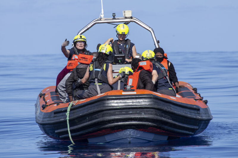 RHIB Crew mit gelben Helmen auf einem Schnellboot zusammen mit Geretteten