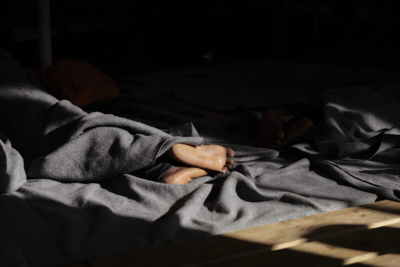 Füße gucken unter einer grauen Decke hervor und werden teilweise von der Sonne bestrahlt.