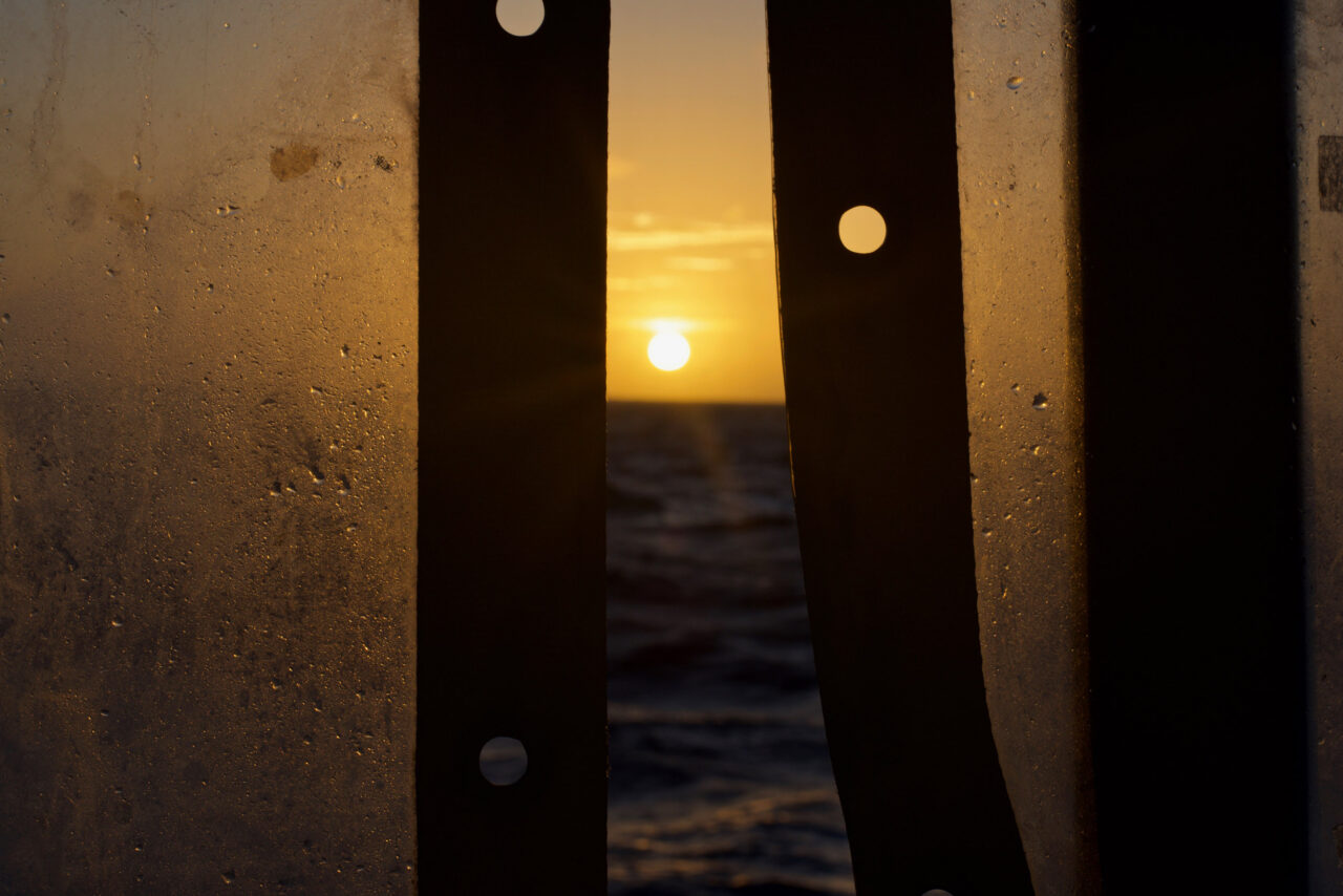 Blick auf die aufgehende Sonne hinter dem Mittelmeer zwischen zwei Planen der Humanity 1.