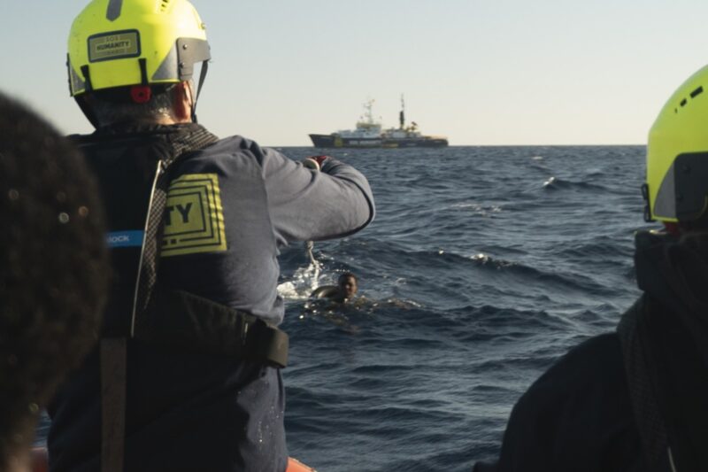 Zwei Crewmitglieder auf einem RHIB von hinten bei der Rettung einer Person, die sich im Wasser befindet.