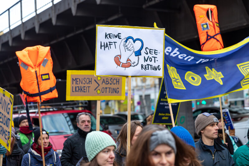 Menschen bei einer Demonstration in Berlin mit den Schildern "Keine Haft für Seenotrettung" und "Leben retten ist Pflicht"