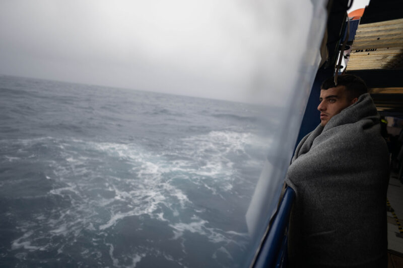 In Decke gehüllter Geretteter blickt aus der Humanity 1 auf das stürmische Mittelmeer.