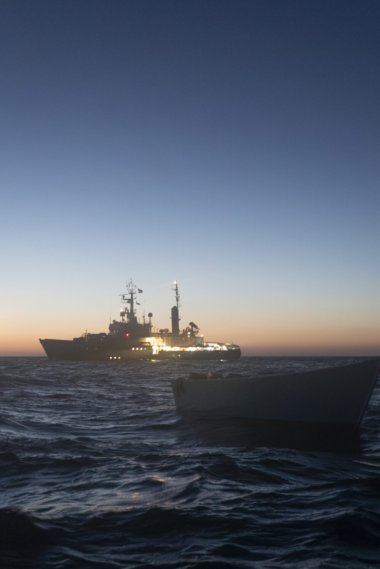 Foto von einem Holzboot vor der Humanity 1 in der Dämmerung auf dem Mittelmeer.