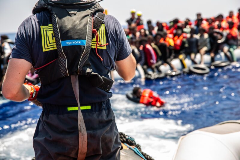Crew member of SOS Humanity looks at a rubber boat with lots of people - some are already in the water.