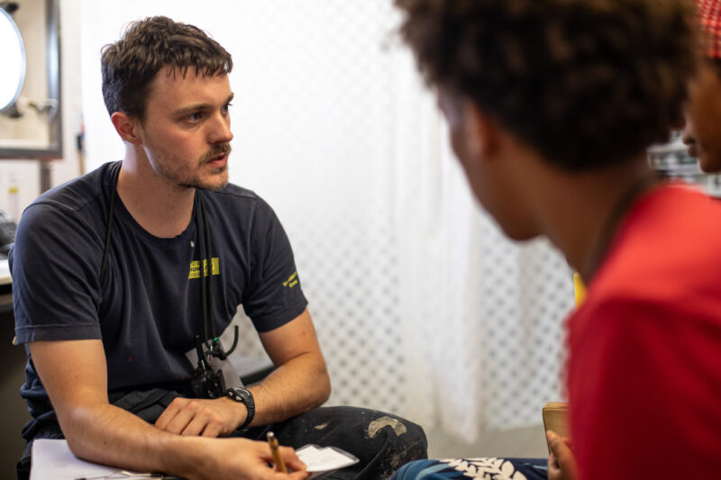 zwei Gerettete und ein Crew-Member sitzen sich gegenüber und sprechen miteinander