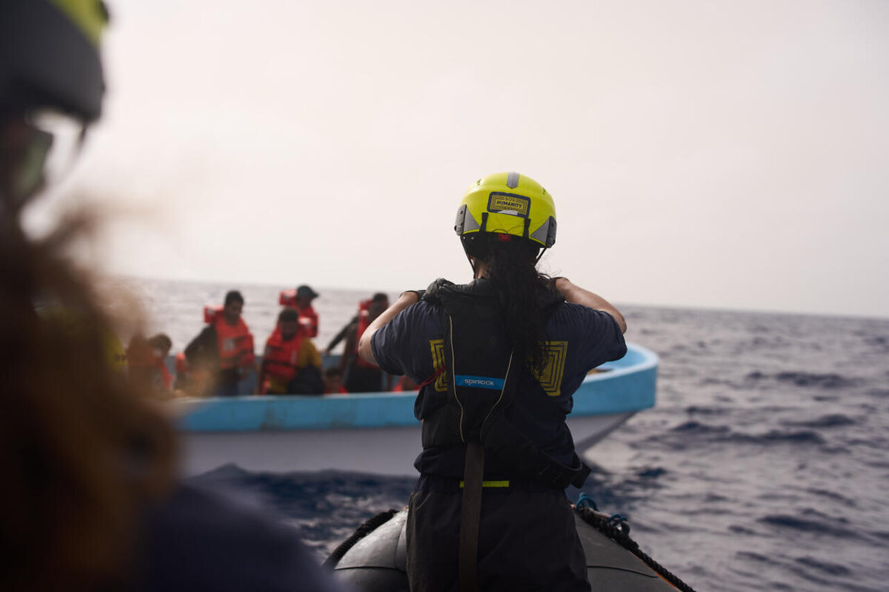 Eine Person mit Sicherheitshelm fährt das RHIB, das Schnellboot, um ein Boot mit Menschen aus Seenot zu retten.