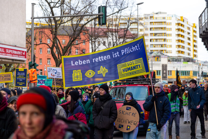 Foto einer Demonstration in Berlin mit vielen Menschen und einem großen, blau-gelben Banner mit der Aufschrift "Leben retten ist Pflicht" von SOS Humanity.