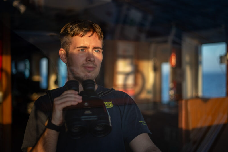 Louis, der Menschenrechtsbeobachter an Bord der Humanity 1 mit einem Fernglas in der Hand