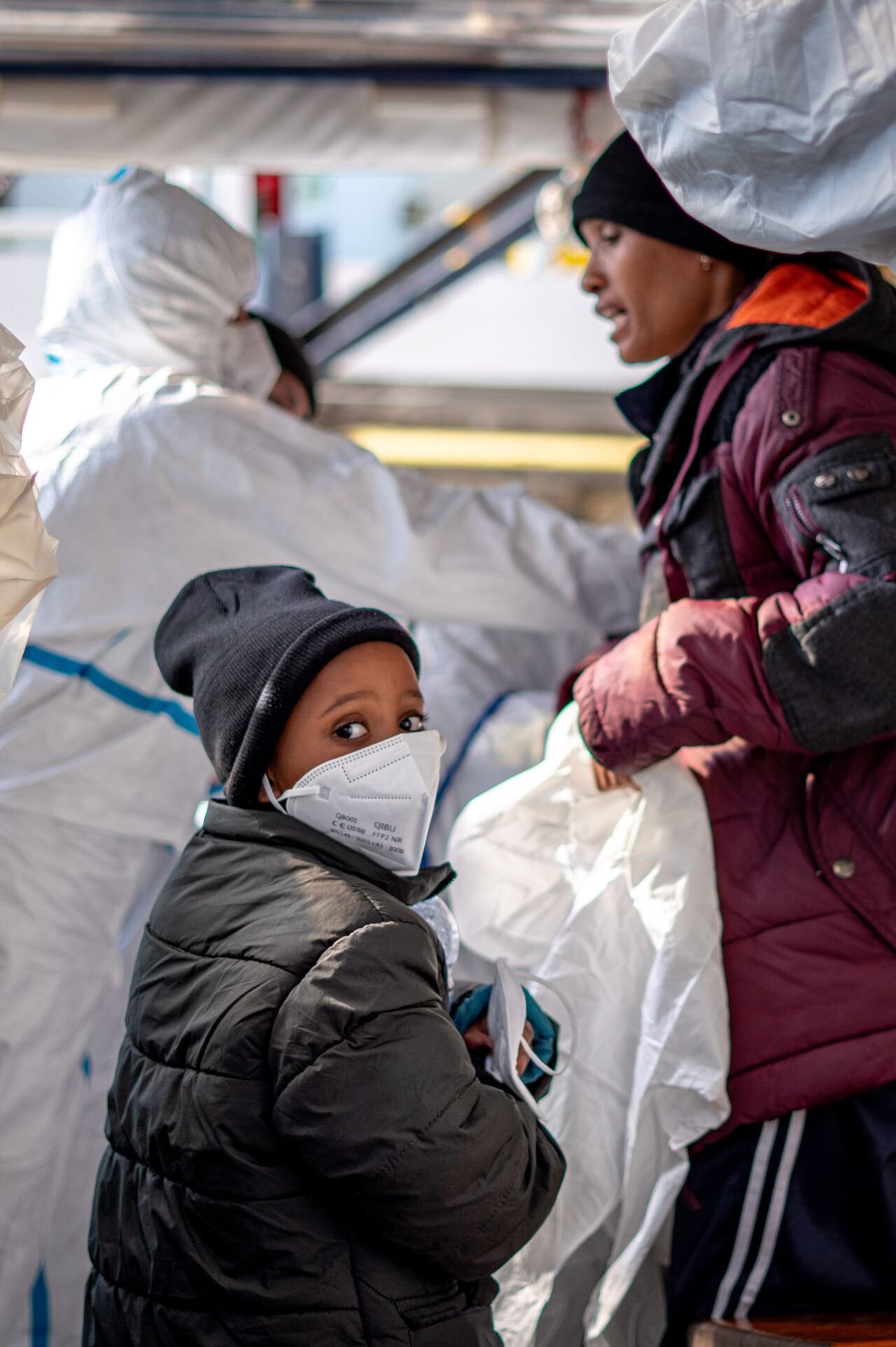 Ein gerettetes Kind trägt eine FFP2-Maske und blickt mit großen Augen nach hinten. Das Foto wurde kurz vor der Disembarkation aufgenommen.