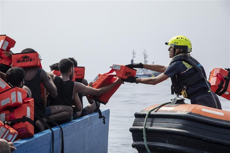 Rettungssituation mit einem Crewmitglied von SOS Humantiy, das Flüchtlingen auf einem Boot Rettungswesten reicht.