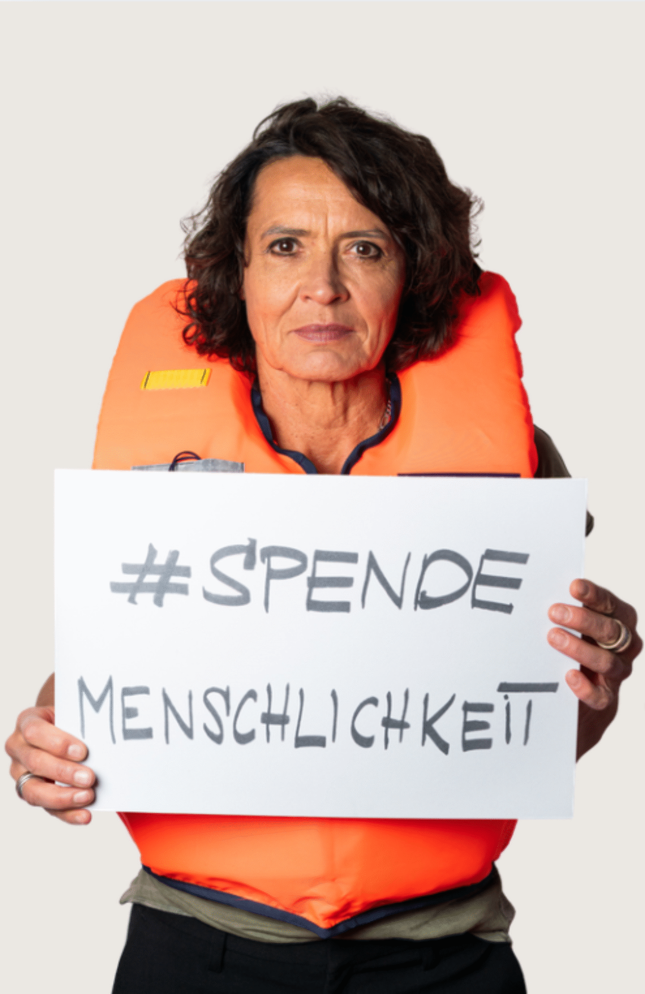 Ulrike Folkerts mit einer Rettungsweste und dem Schild 'SPENDEMENSCHLICHKEIT