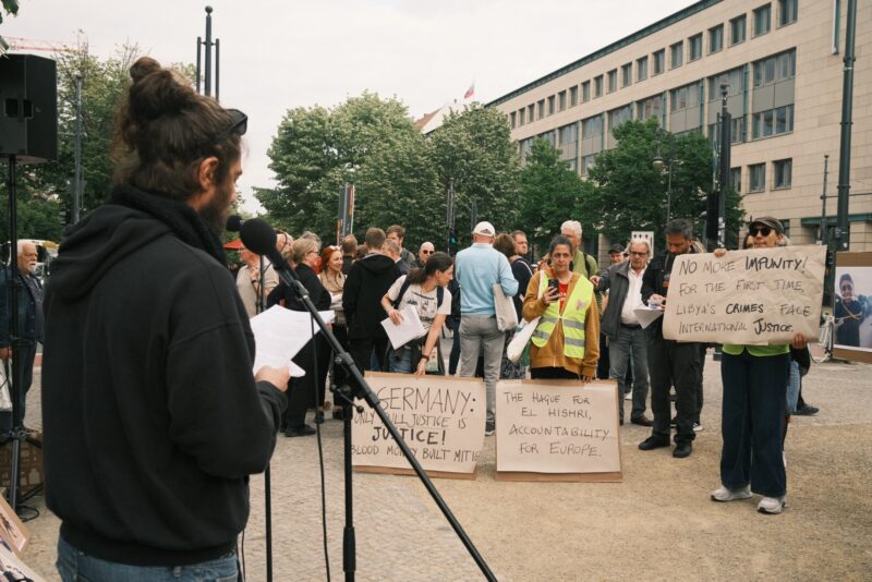 A man is holding a speech at a demonstration and people are holding signs listening to him.